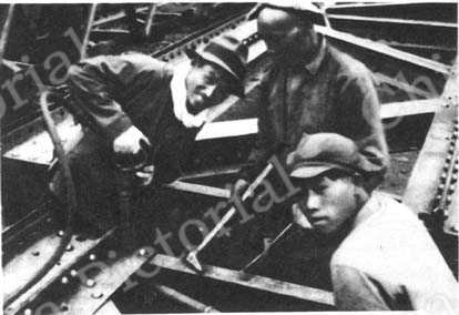 
天津制钢厂生产模范徐敬生利用废材做了三百四十多种器材，图为他和工人们在做新的马丁炉钢架。
